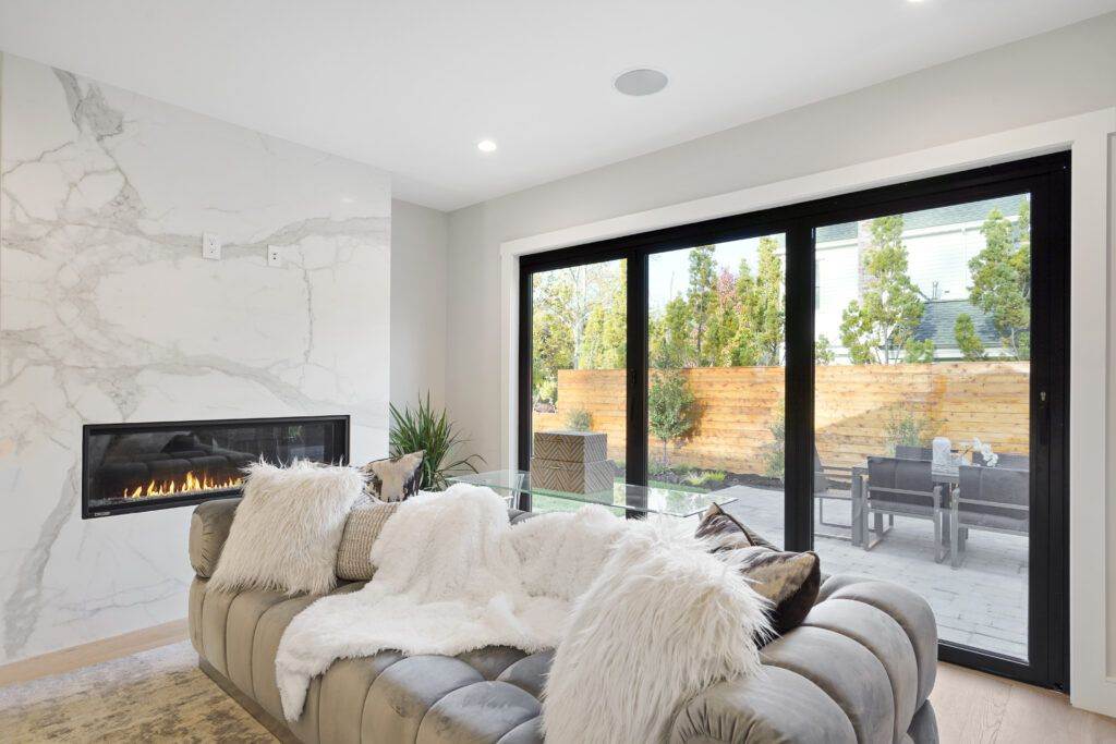 Modern living room with a large sofa covered in a fur blanket, showcased in a construction portfolio, featuring marble walls and sliding glass doors leading to an outdoor patio.