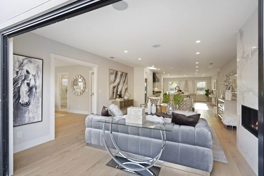 Modern living room with gray sectional sofa, glass coffee table, and a post-construction fireplace. Decor includes wall art and a mirrored clock.