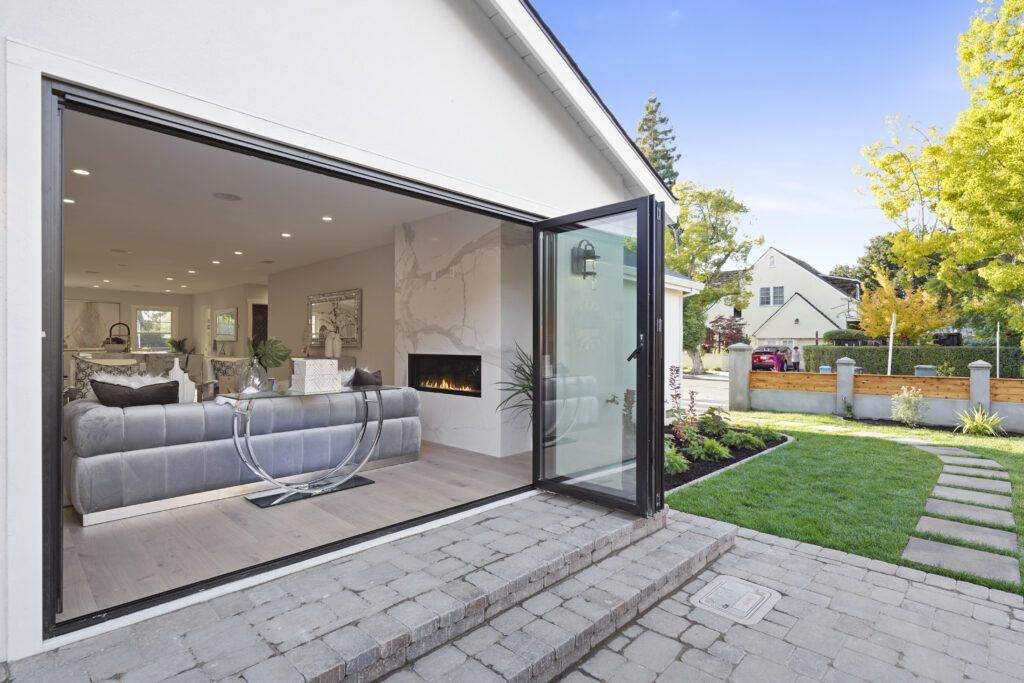 Modern living room visible through large open sliding glass doors, featuring a gray sofa, fireplace, and a minimalist decor, with a landscaped garden outside. This scene is part of our post-construction portfolio