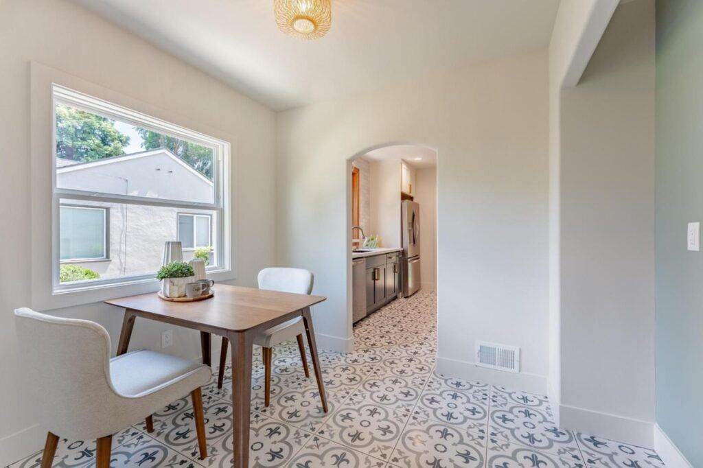 Bright dining area with a wooden table, two chairs, decorative floor tiles, and windows showing external greenery, perfect for a construction portfolio.