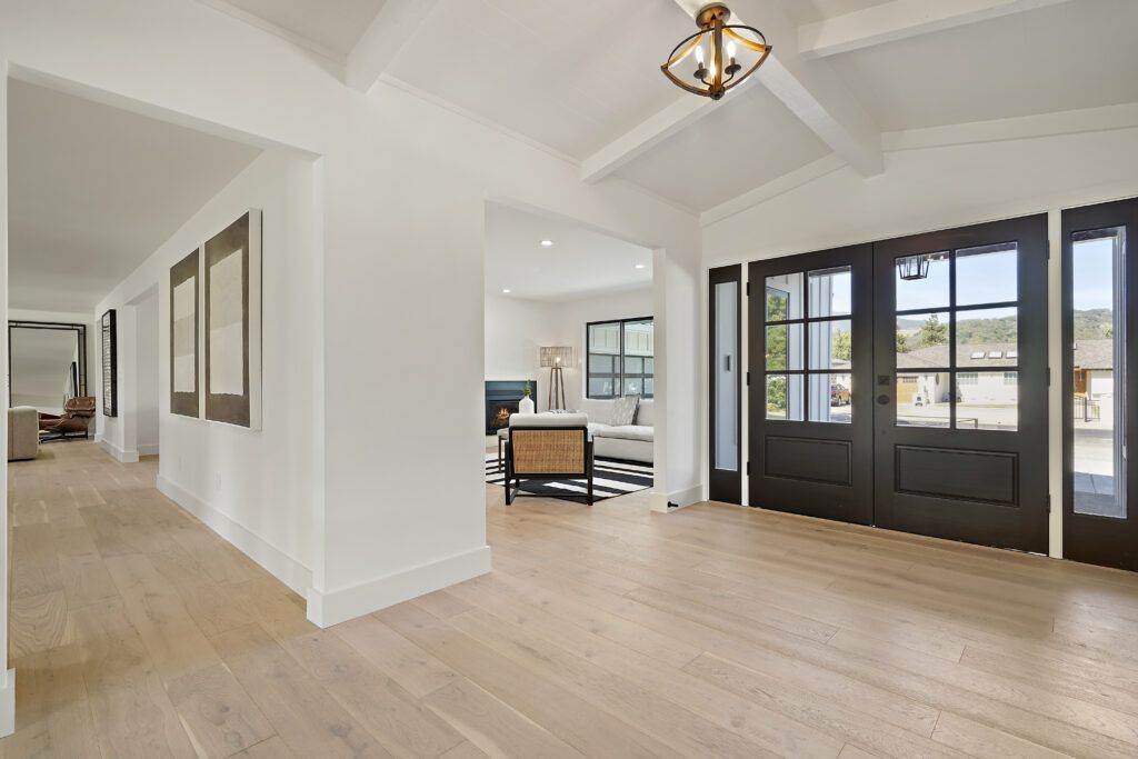 Bright, modern hallway with wooden floors, white walls, and black framed doors leading to an elegantly furnished room in a post-construction portfolio.