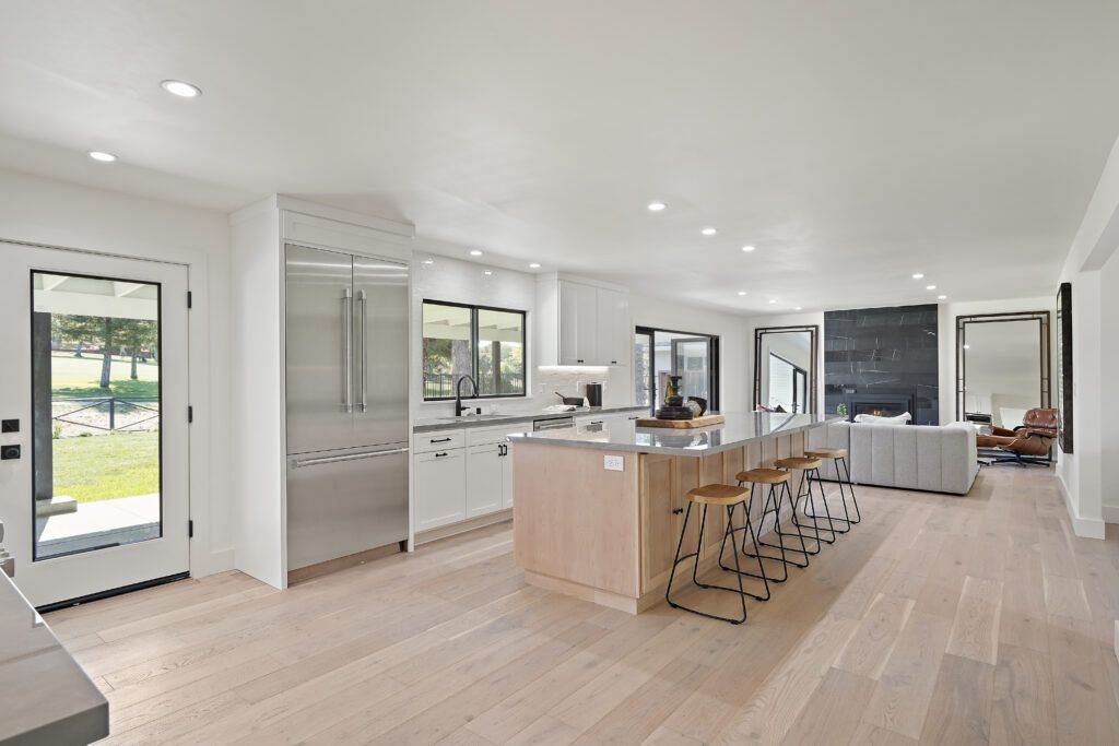 Modern kitchen interior featured in our construction portfolio, with stainless steel appliances, white cabinets, a central island with bar stools, and open plan layout leading to a living area.