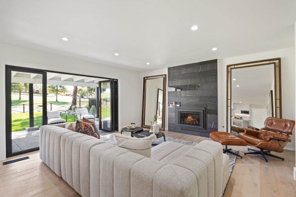 Modern living room with a gray sofa, leather chair, fireplace, and sliding glass doors opening to a garden, featured in a construction portfolio.