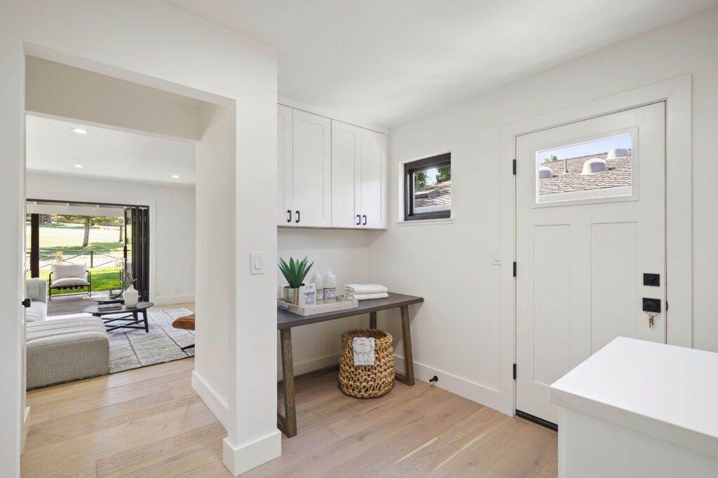 Modern home entryway, featured in a post-construction portfolio, with a white door, a small table with decorative plants, a woven basket, and a view into a living room with large windows.