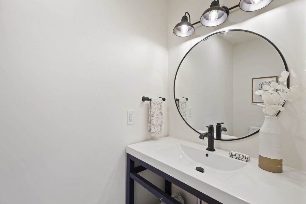 Modern bathroom featuring a navy blue vanity with a white countertop, a round mirror, and black fixtures, accented by a white vase with post-construction flowers.