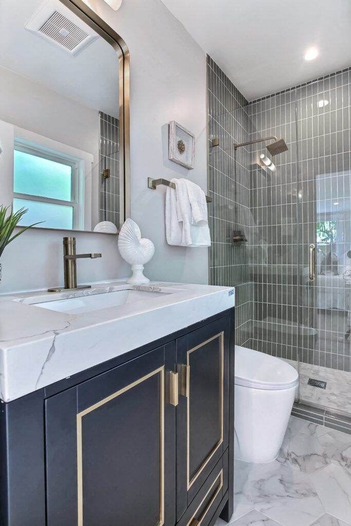 Modern bathroom from our construction portfolio features a navy blue vanity, marble countertop, and mirrored wall tiles. White fixtures and gold accents complete the clean, contemporary look.