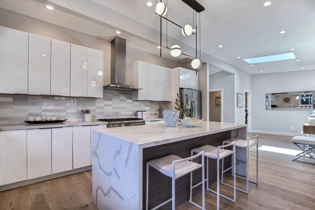 Modern kitchen interior with white cabinetry, marble countertops, and a central island with bar stools, showcased in our construction portfolio.