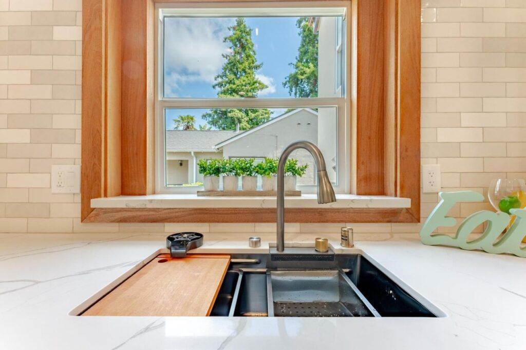 Kitchen sink with a cutting board, facing a window overlooking a suburban house and trees under a blue sky, featured in a post-construction portfolio.