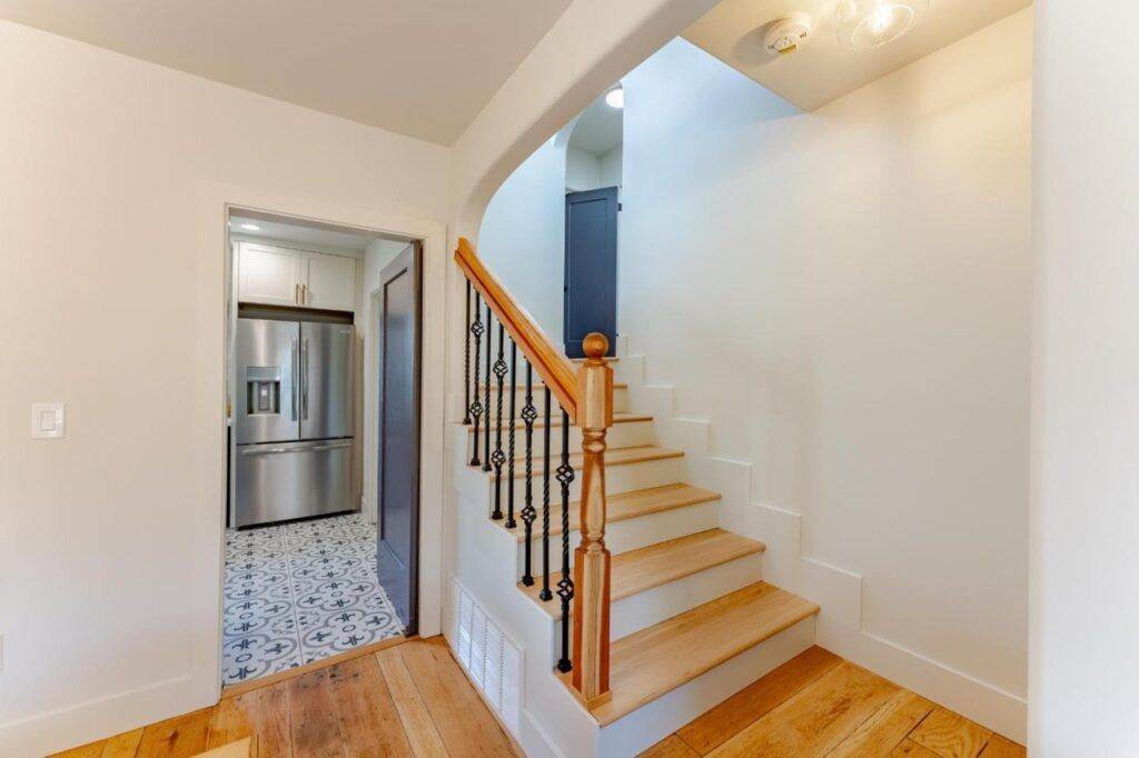 A home interior featuring a staircase with wooden railings leading up beside a kitchen entrance with patterned flooring, perfect for a construction portfolio showcase.