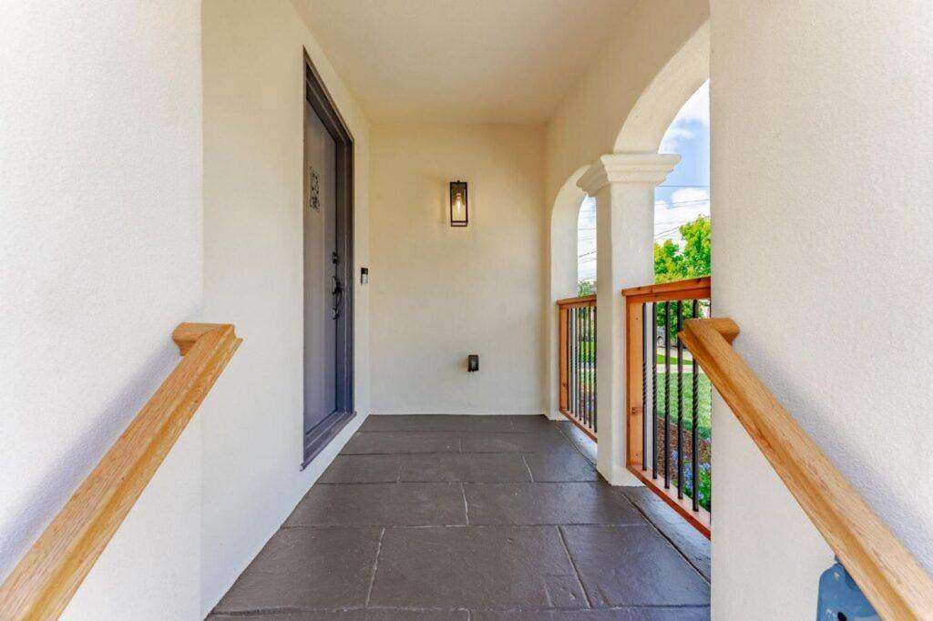 Bright, covered porch with a slate floor, arched openings, a wooden railing, and a dark front door in a post-construction entryway.