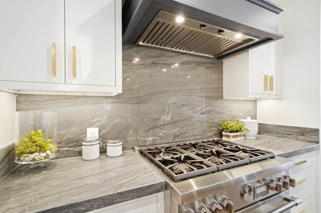 Modern kitchen with white cabinets, stainless steel stove, and gray marble backsplash and countertops, featured in our post-construction portfolio.