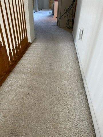 A narrow hallway in a house with textured beige carpeting, white walls, and a wooden door on the left, leading to a room prepared for master clean service.