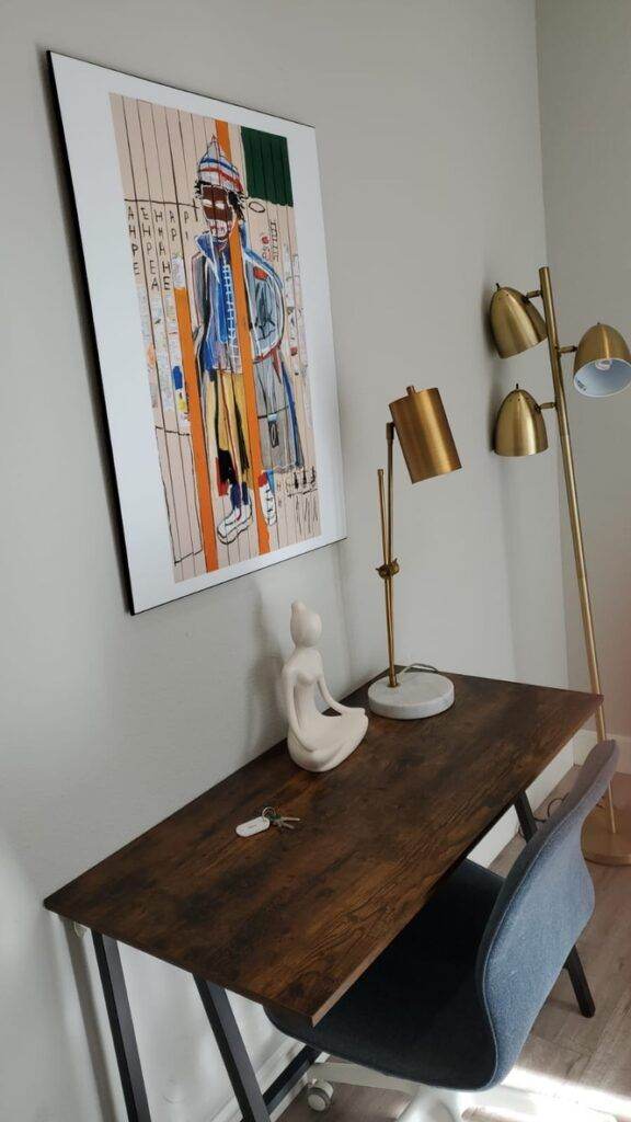 A modern home office with a wooden desk, a blue chair serviced by Newark Upholstery Cleaning, a gold floor lamp, and a framed abstract art piece on the wall.