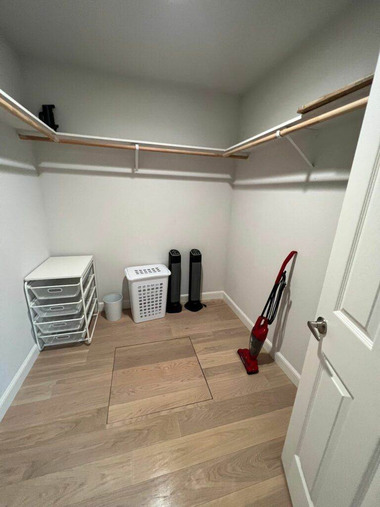 A small, tidy closet with wooden floors, featuring a vacuum cleaner from Newark Short Term Cleaning, storage drawers, and a clothes rack with shelves.