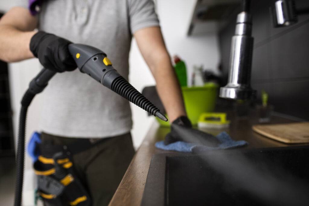 A person wearing gloves uses a steam cleaner to sanitize a kitchen sink, exemplifying the meticulous attention to detail provided by Master Clean's professional deep cleaning services in San Jose.