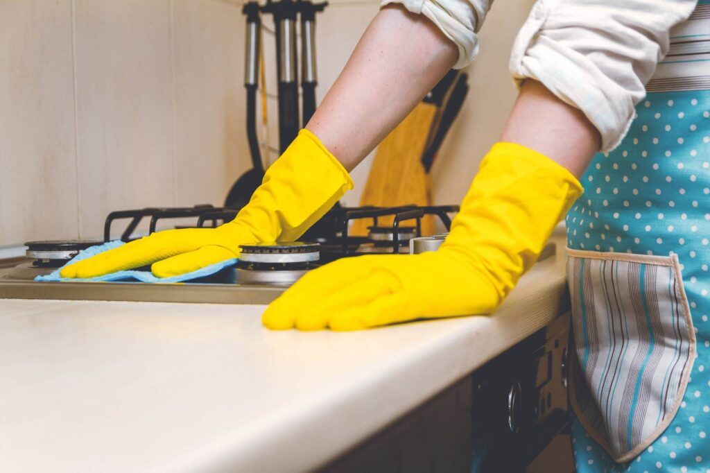 In Palo Alto, a person wearing yellow rubber gloves and a blue apron diligently cleans a kitchen stove with a blue microfiber cloth, making sure to keep every surface Kitchen Spotless.