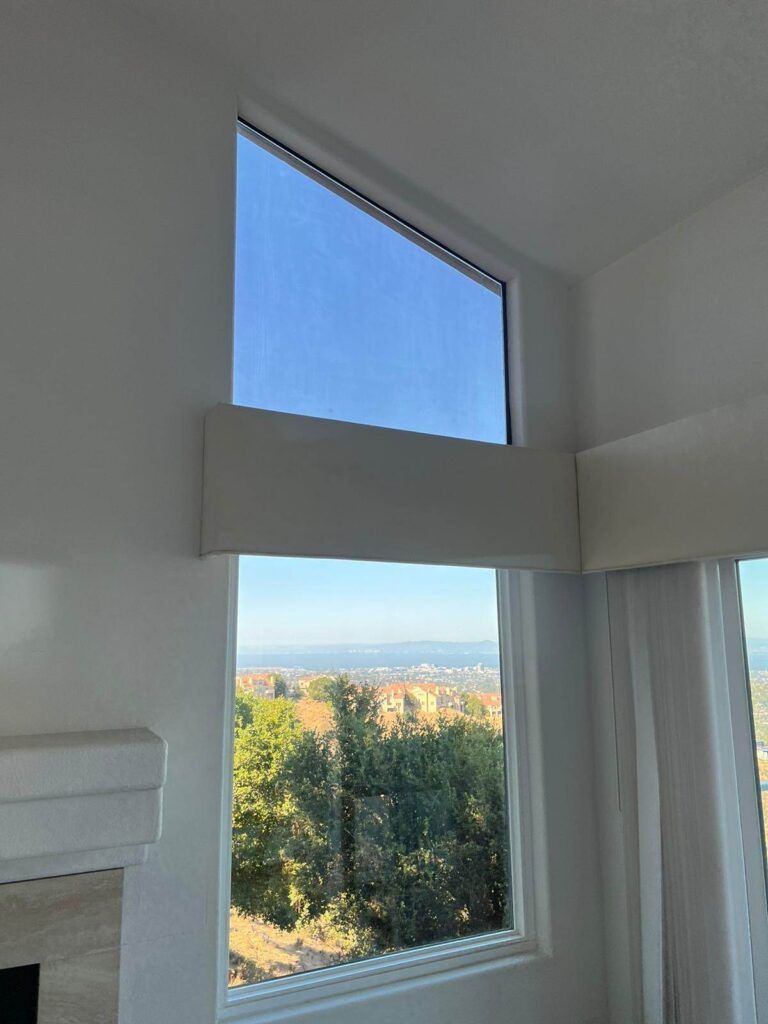 View from an indoor corner window showing a landscape with trees and a distant cityscape under a clear blue sky.