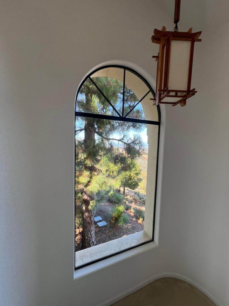 An arched window with a view of a pine tree outside. A wooden lantern hangs from the ceiling nearby.