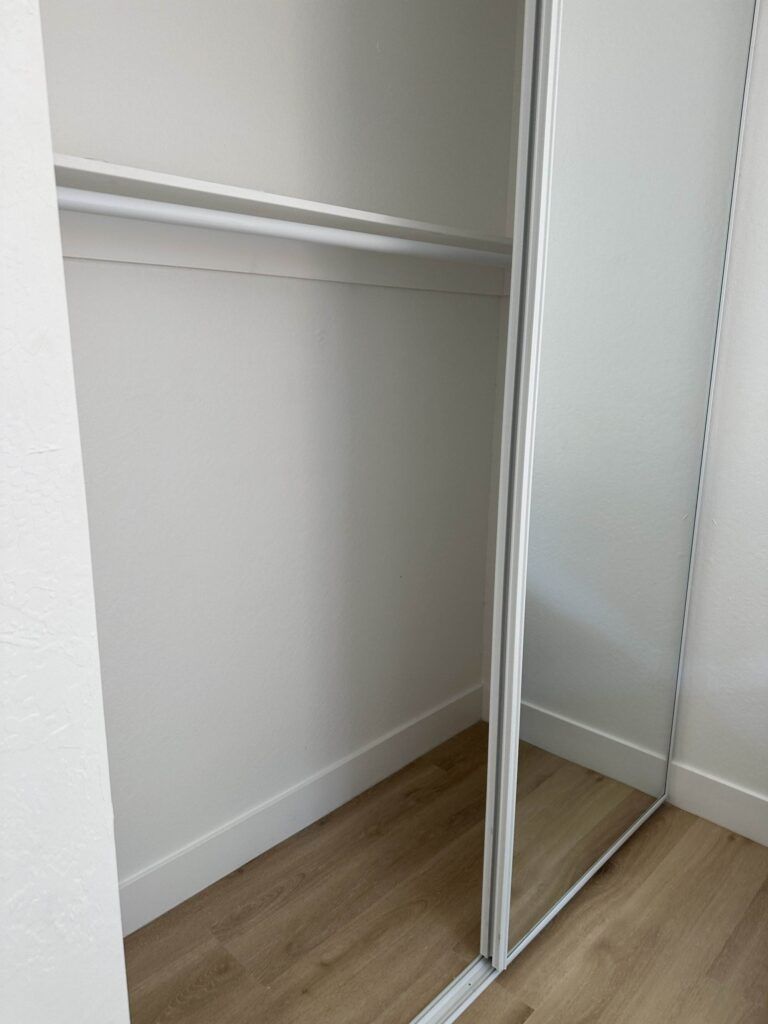 An empty closet with sliding mirror doors, beige walls, and a wooden floor.