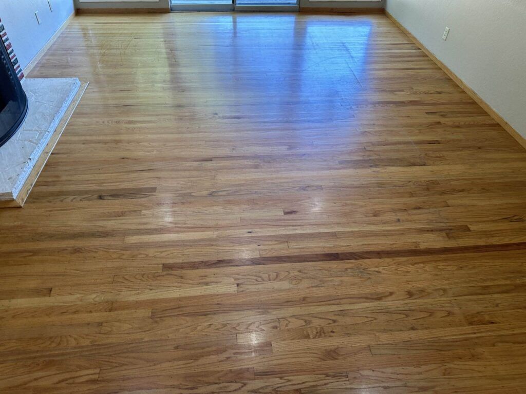 A room with polished hardwood floors, a fireplace on the left, and a sliding glass door at the far end. The walls are painted a light color.