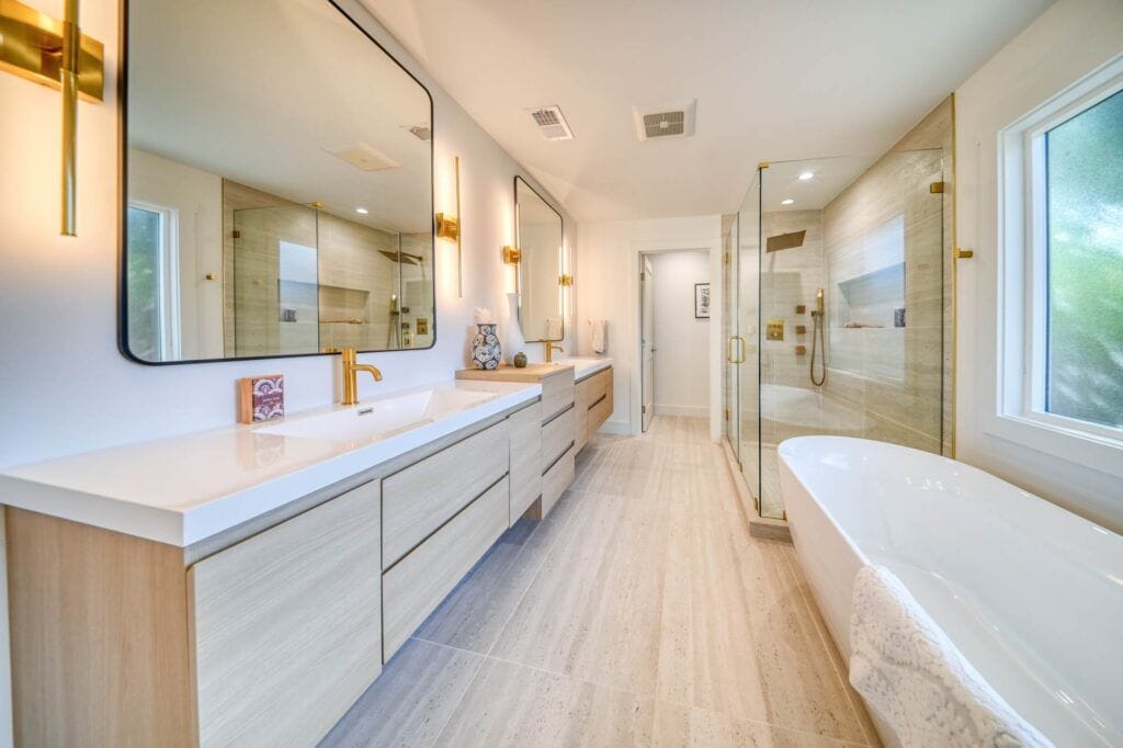 A modern bathroom featuring a long double vanity with two large mirrors, a freestanding bathtub, and a glass-enclosed shower. Neutral tones and gold fixtures create a sleek and stylish look.