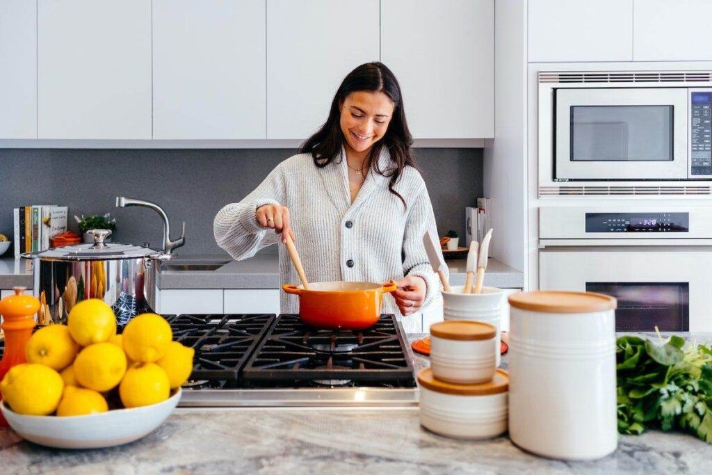 A person stirs food in a pot on a kitchen stove, surrounded by containers and a bowl of lemons, creating a scene straight out of an ApartmentGuide featured article.