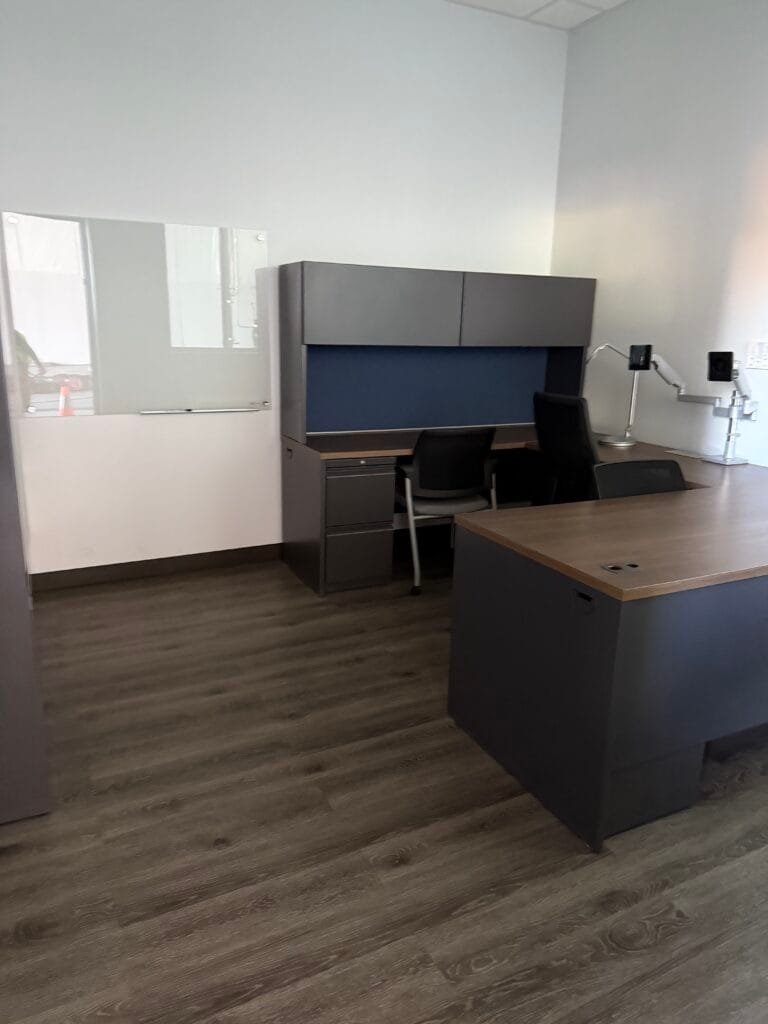 Modern office with two desks, black chairs, a whiteboard, and light wood flooring. The minimally furnished, well-lit room highlights the results of professional janitorial cleaning services.
