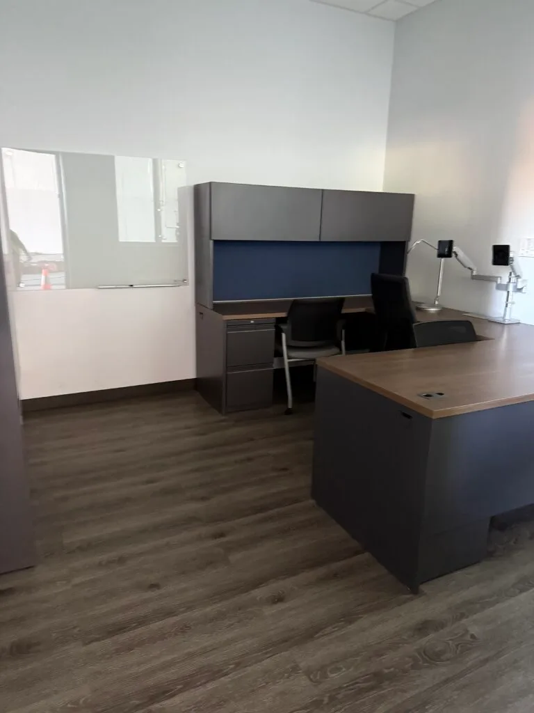 Modern office with two desks, black chairs, a whiteboard, and light wood flooring. The minimally furnished, well-lit room highlights the results of professional janitorial cleaning services.