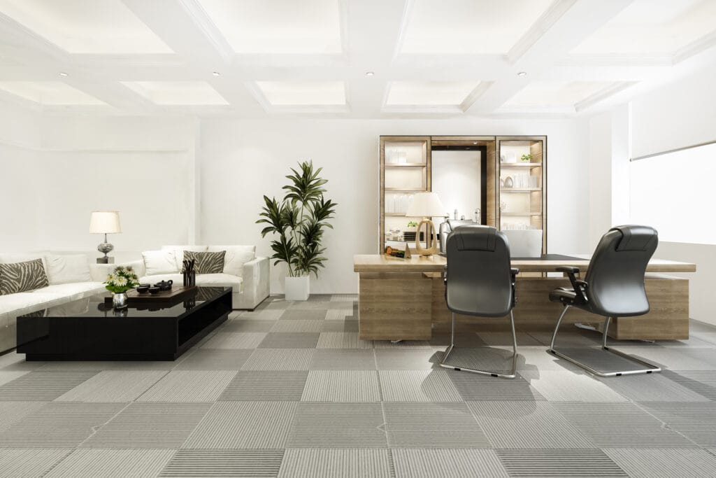Modern office in Los Gatos featuring a wooden desk, two black chairs, a white sofa set, coffee table, potted plants, and shelves in a bright room—ideal for professional office care and janitorial cleaning.