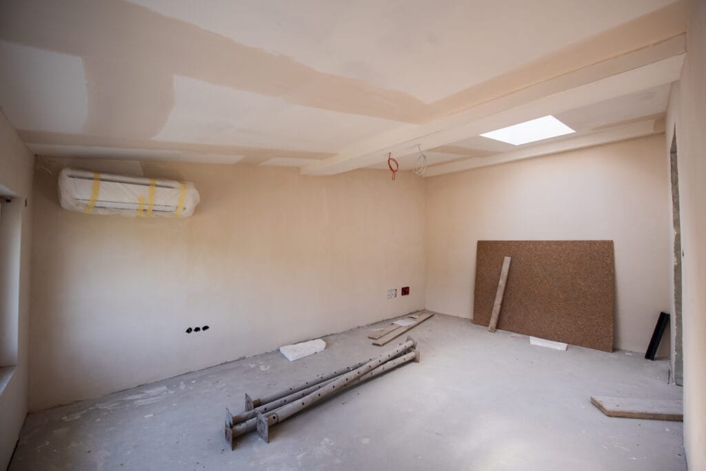 Unfinished room with bare plastered walls, construction materials on the floor, exposed wiring, and a skylight in the ceiling—ideal for builders or those seeking partial renovation cleaning in Santa Clara.