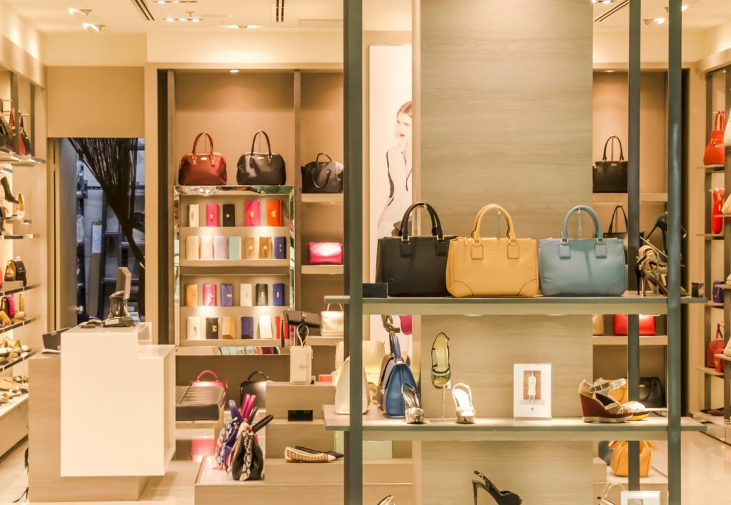 Handbags and shoes are displayed on shelves and tables inside a brightly lit boutique store, freshly organized after a final cleaning by expert builders in San Jose.
