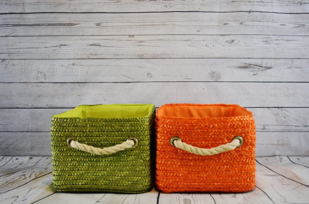 Two square storage baskets with rope handles, one green and one orange, sit side by side on a wooden floor—perfect for Santa Clara County homeowners looking to stay organized after a roommate move-out cleaning.