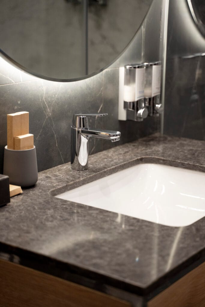 Modern bathroom sink with a marble countertop, chrome faucet, wooden and ceramic containers, and wall-mounted soap dispensers—ideal for Property Managers in Cupertino seeking effortless bathroom cleaning solutions.