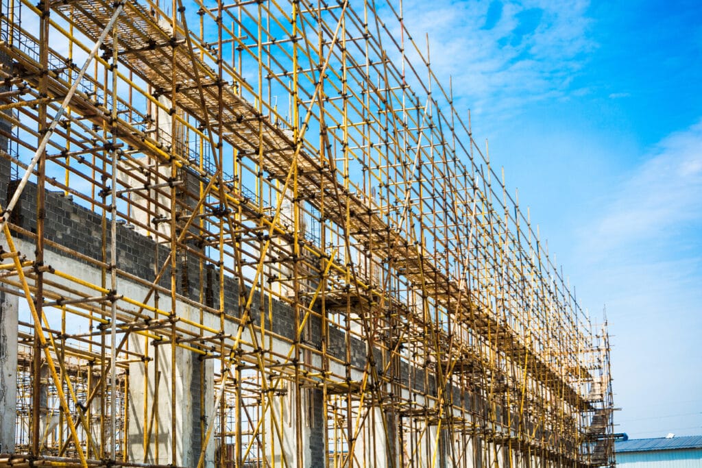 A large construction site with extensive metal scaffolding surrounds a multi-story building frame against a blue sky, perfect for Saratoga post-construction cleaning before the space is ready for use.