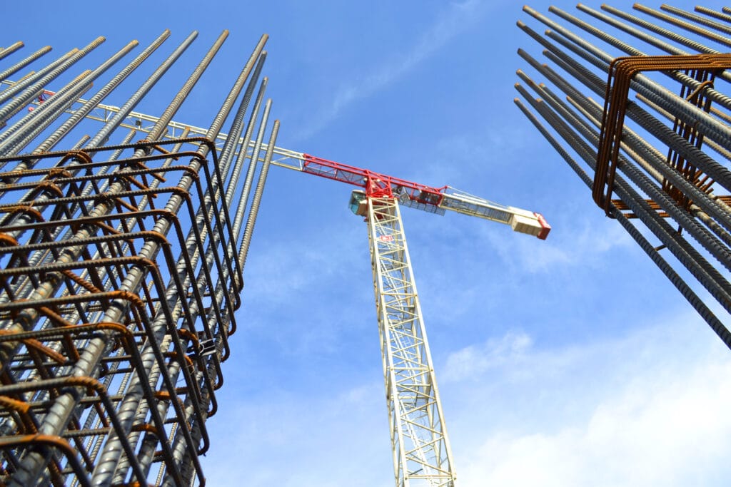A red and white construction crane stands between two steel rebar structures under a clear blue Saratoga sky, marking progress before homeowners arrive for post-construction cleaning.