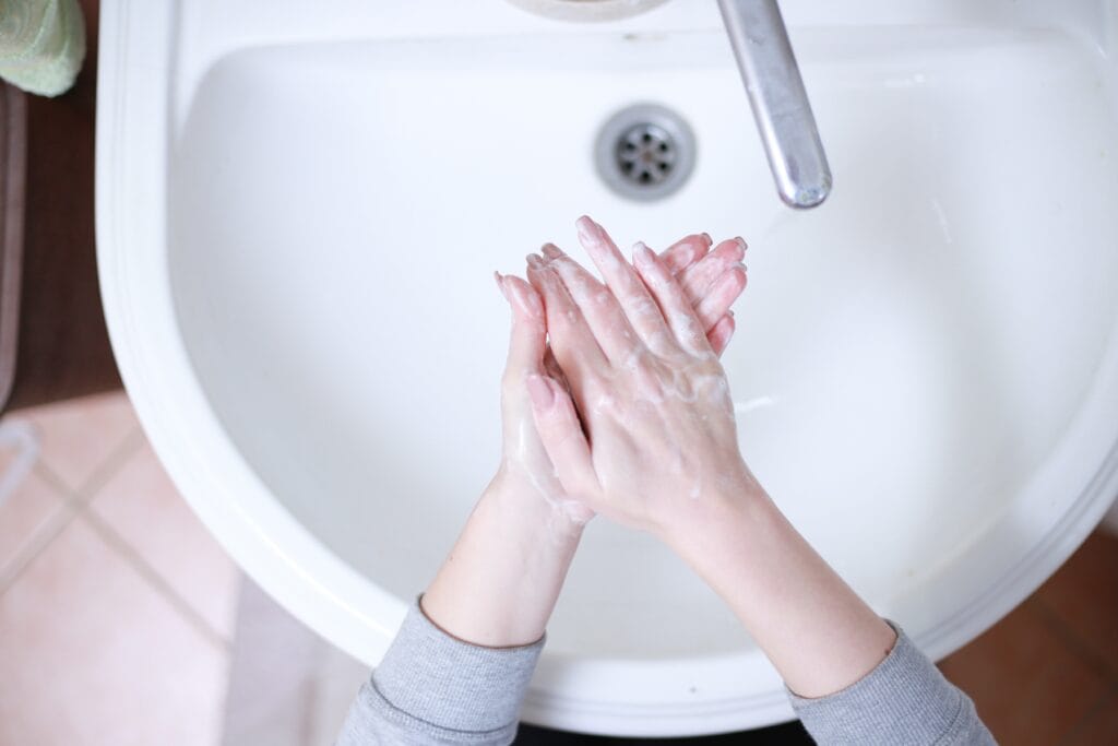 Person washing hands with soap at a white sink in a Los Gatos home, highlighting the importance of bathroom cleaning; the water faucet is visible above the hands.