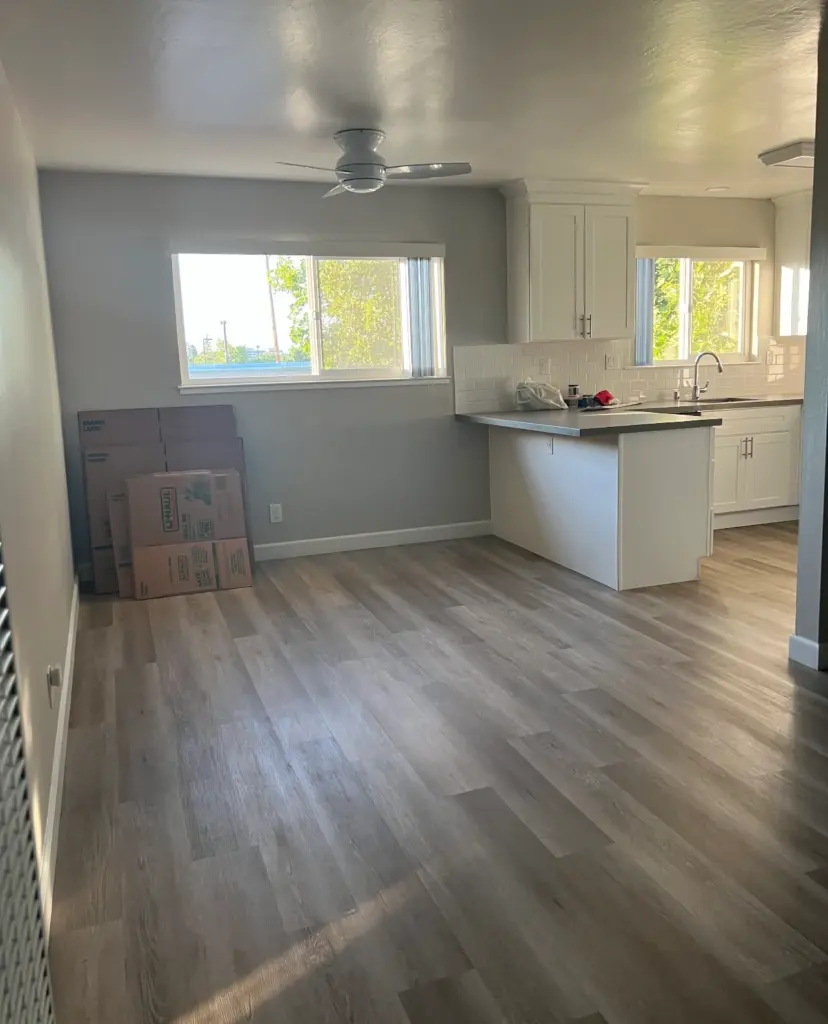 Bright San Jose apartment with light wood floors, a kitchen featuring white cabinets, ceiling fan, and moving boxes by the window—perfect space to refresh with professional janitorial cleaning from Office Care.