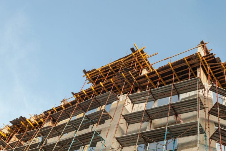 A partially constructed building with scaffolding and yellow support beams stands against a clear blue sky, awaiting post-renovation remodel cleaning in Santa Clara County.