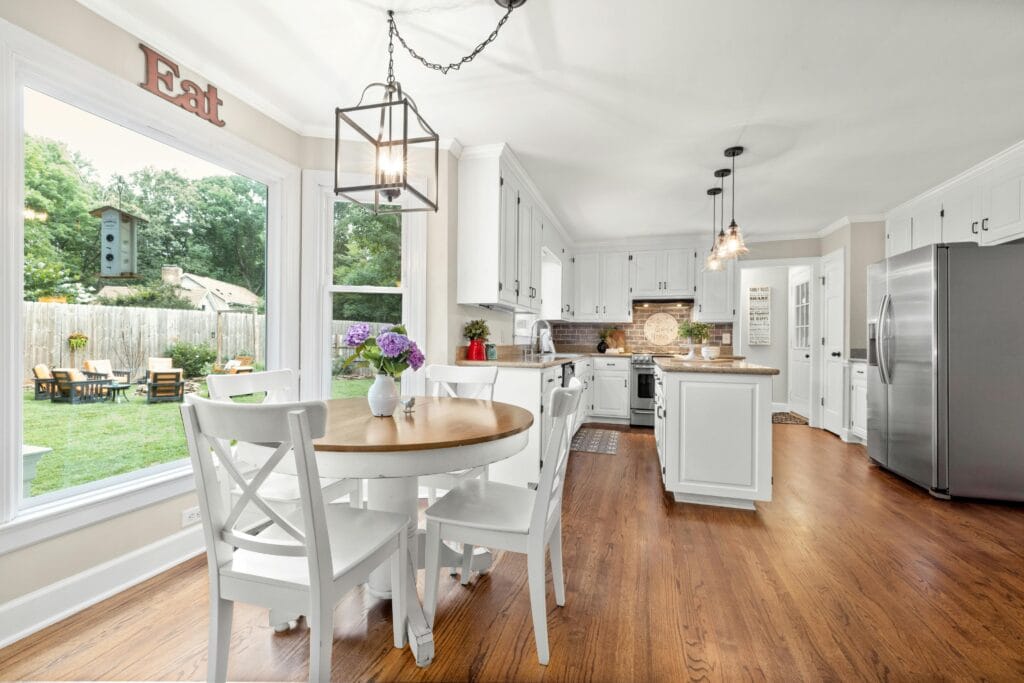 Bright kitchen with white cabinets, stainless steel appliances, and a round dining table for four. Large window overlooks the backyard with patio furniture—freshly prepared by builders and jobsite ready after final cleaning in Cupertino.