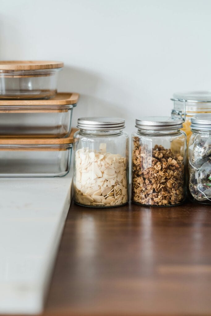 Glass jars filled with sliced almonds, granola, and more line a wooden countertop in a Campbell home, reflecting the benefits of customized kitchen cleaning for organized shared spaces. Stacked glass containers with wooden lids add a tidy finish.