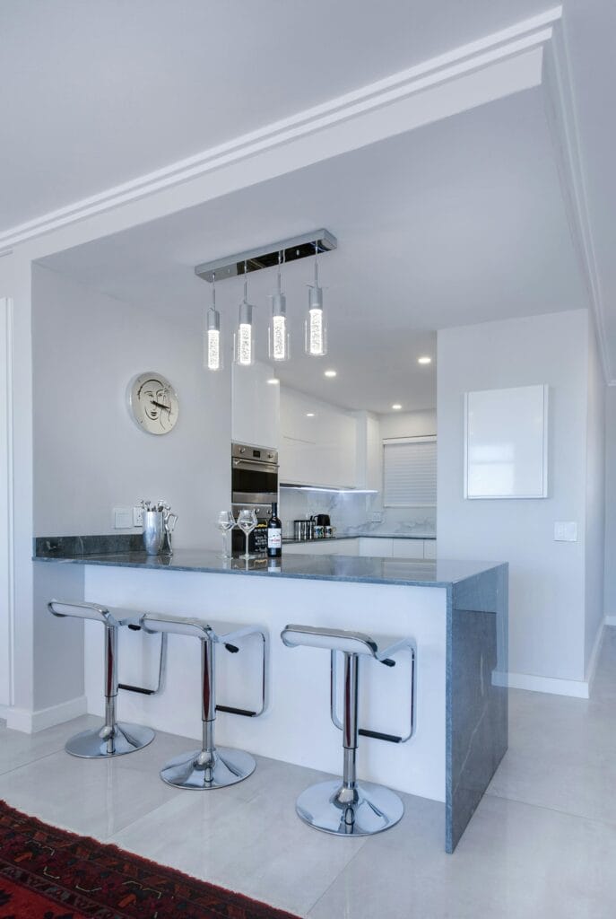 Modern Campbell kitchen with a grey stone island, three chrome bar stools, built-in oven, minimalist white cabinets, and pendant lights—perfect for effortless kitchen cleaning in shared spaces.