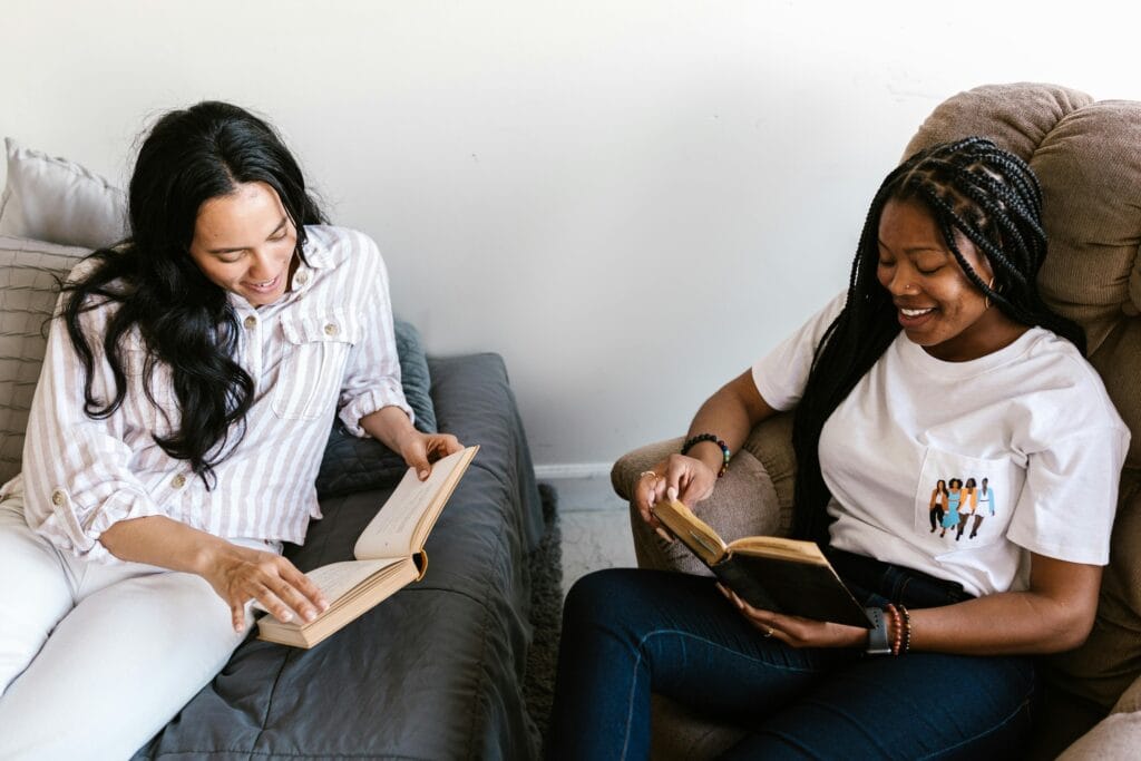 Two women, likely homeowners, sit indoors reading books and smiling—one on a couch, the other in an armchair—in a cozy Santa Clara County home.