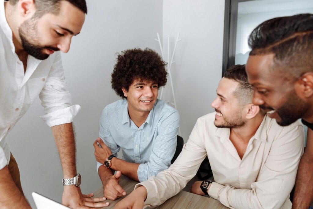 Four men, including office managers, are gathered around a desk in a San Jose office, engaged in conversation and smiling after discussing efficient janitorial cleaning solutions.