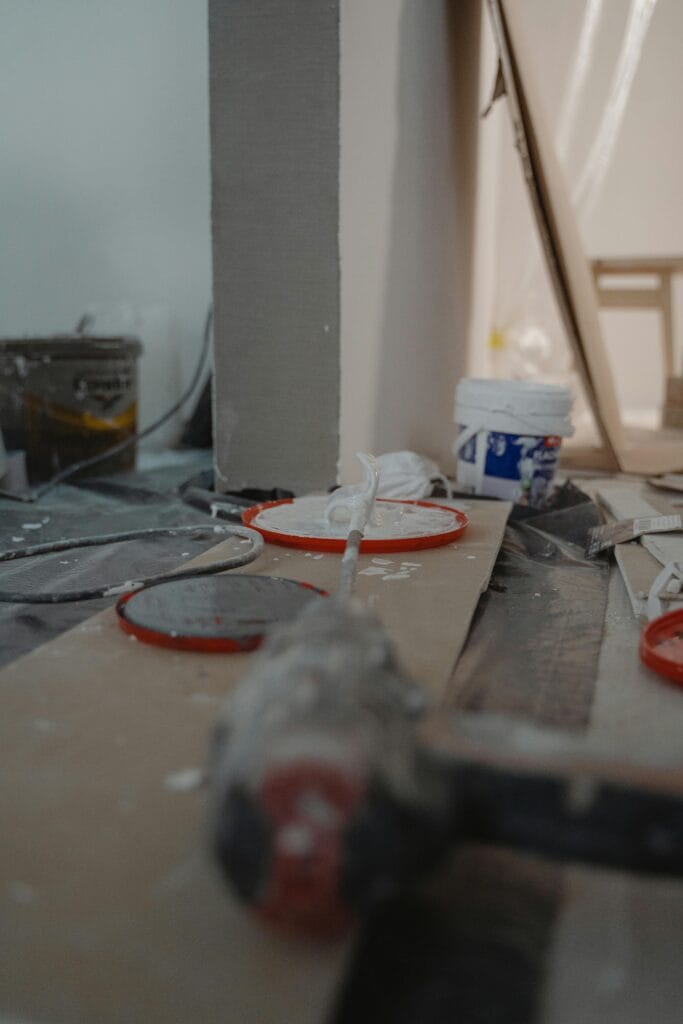A close-up of construction materials and tools on the floor of an unfinished San Jose room, with paint splatters and equipment in the background—perfect for showcasing post-construction cleaning needs.