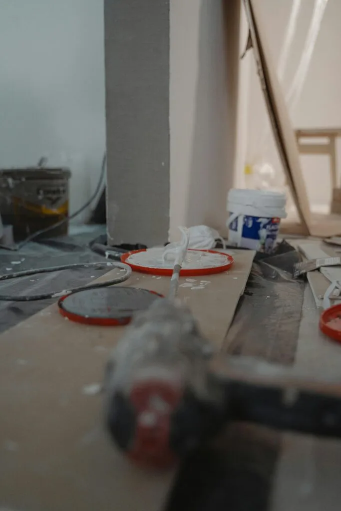 A close-up of construction materials and tools on the floor of an unfinished San Jose room, with paint splatters and equipment in the background—perfect for showcasing post-construction cleaning needs.