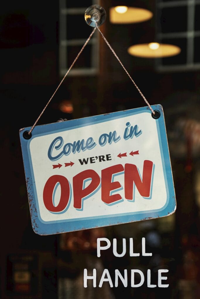 A blue and white sign reading "Come on in, we're OPEN" hangs on a glass door above white text that says "PULL HANDLE," inviting San Jose customers to experience top-notch commercial cleaning.