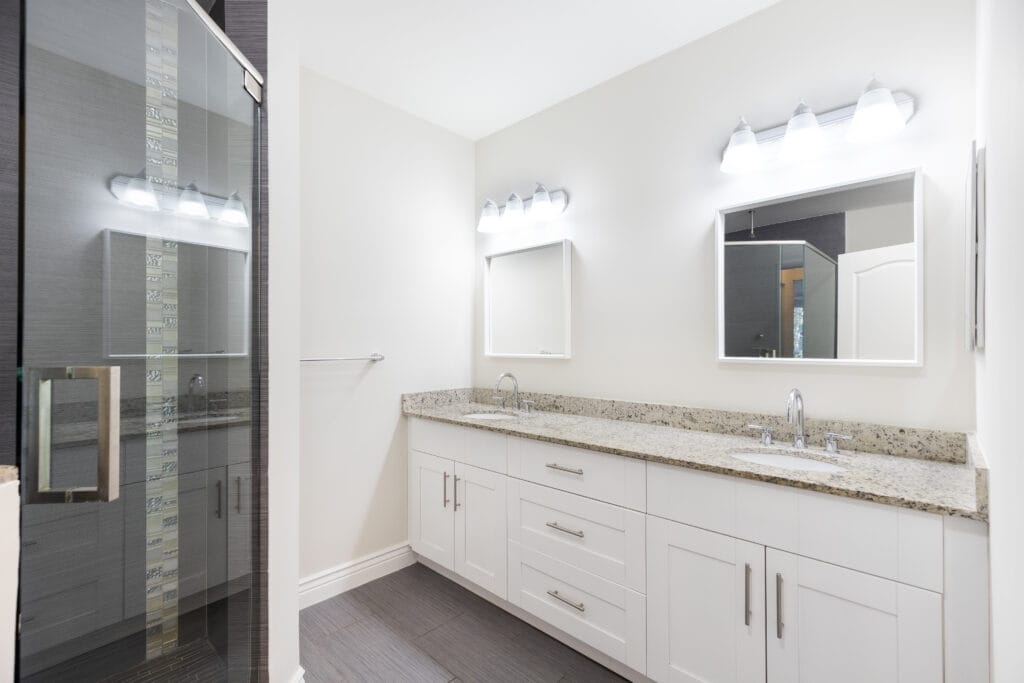 Modern bathroom in San Jose with a glass shower, double sink vanity, granite countertop, white cabinets, and two mirrors under bright lights—perfectly refreshed after expert remodel cleaning.