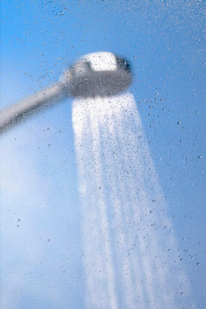 A showerhead spraying water, photographed through a foggy glass surface with droplets—a fresh scene perfect for showcasing Bathroom Deep Cleaning in Santa Clara.
