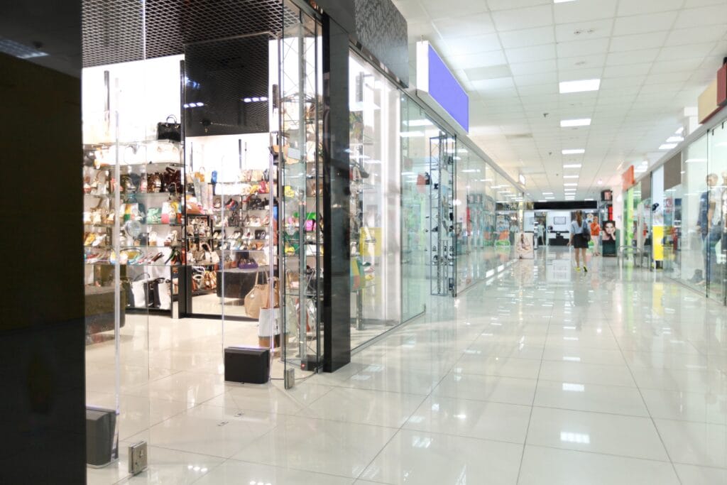 Interior of a Los Gatos shopping mall with glass storefronts, various shops, and bright lighting. A few people are visible walking in the distance, highlighting the pristine look after recent post-construction cleaning.