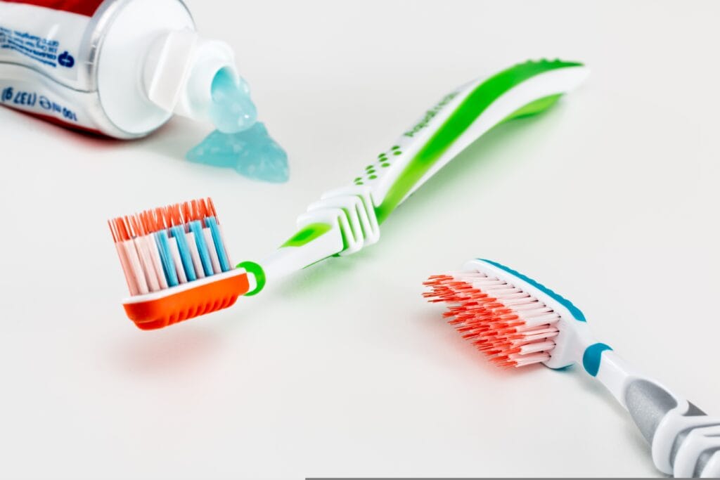 Two toothbrushes and an open tube of blue gel toothpaste are placed on a white surface, with some toothpaste squeezed out—perfect for your customized bathroom cleaning routine in Los Gatos.